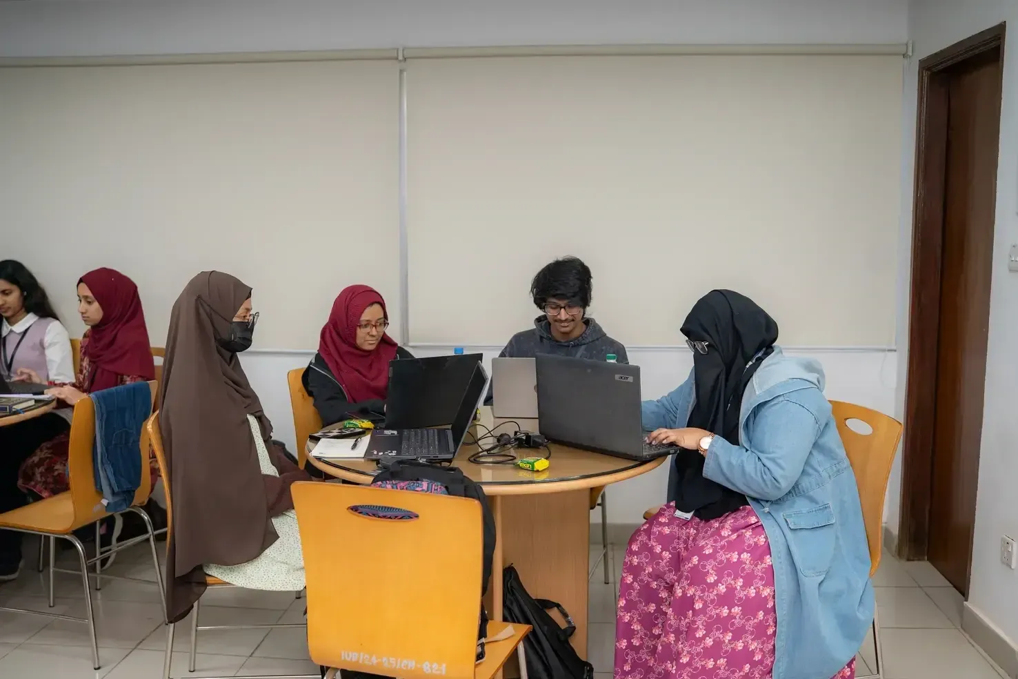 Five workshop participants seated around a table working on laptops.