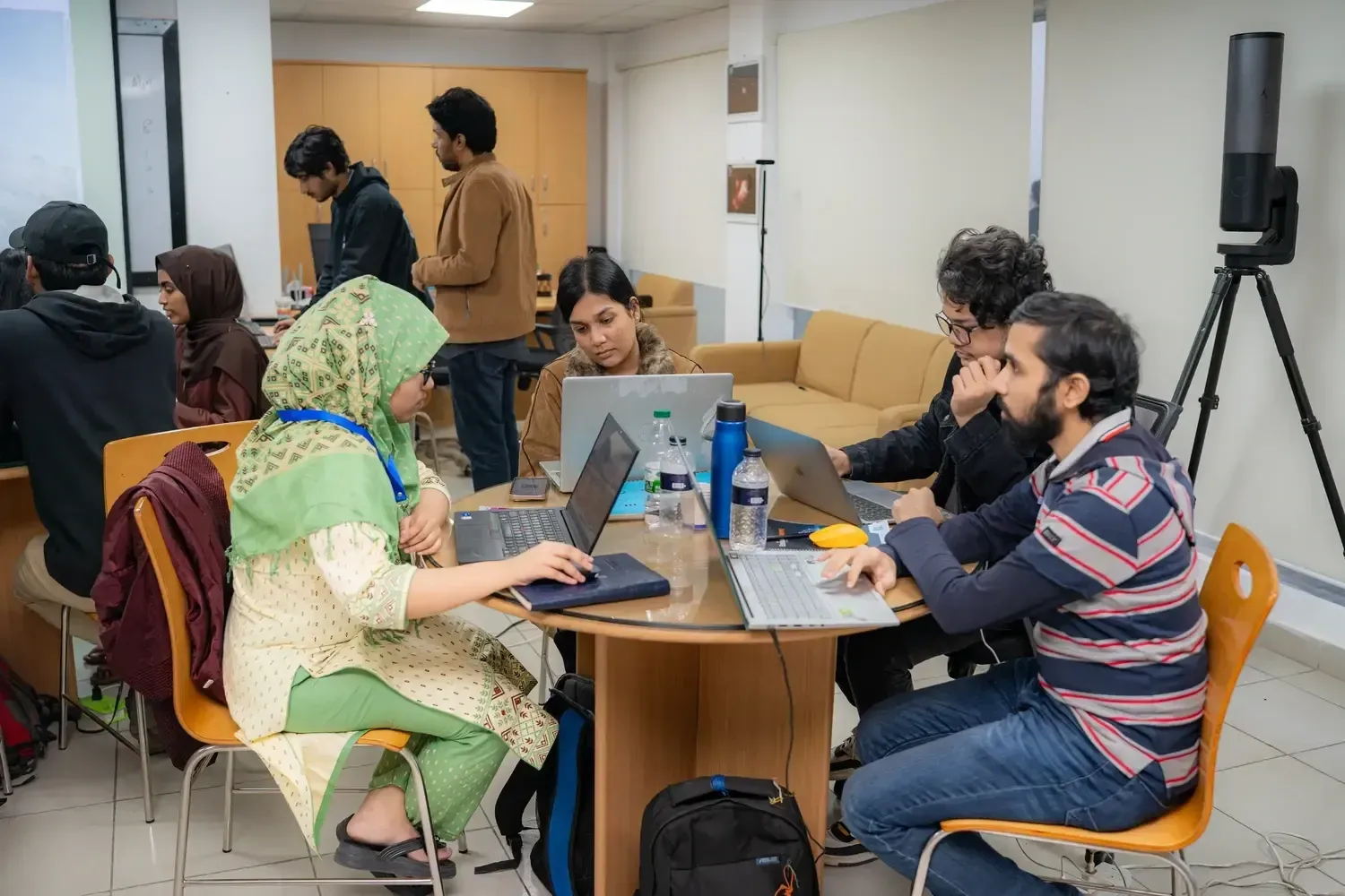 Workshop participants collaborating around tables with laptops, with a telescope on a tripod at the right.