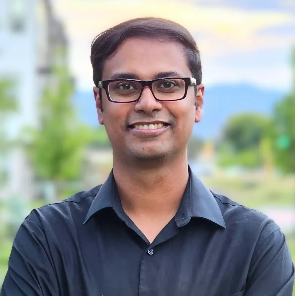 ড. শাহ মোহাম্মদ বাহাউদ্দিনের প্রতিকৃতি — কালো শার্ট পরা, পেছনে ঝাপসা সবুজ গাছপালা ও পাহাড়।