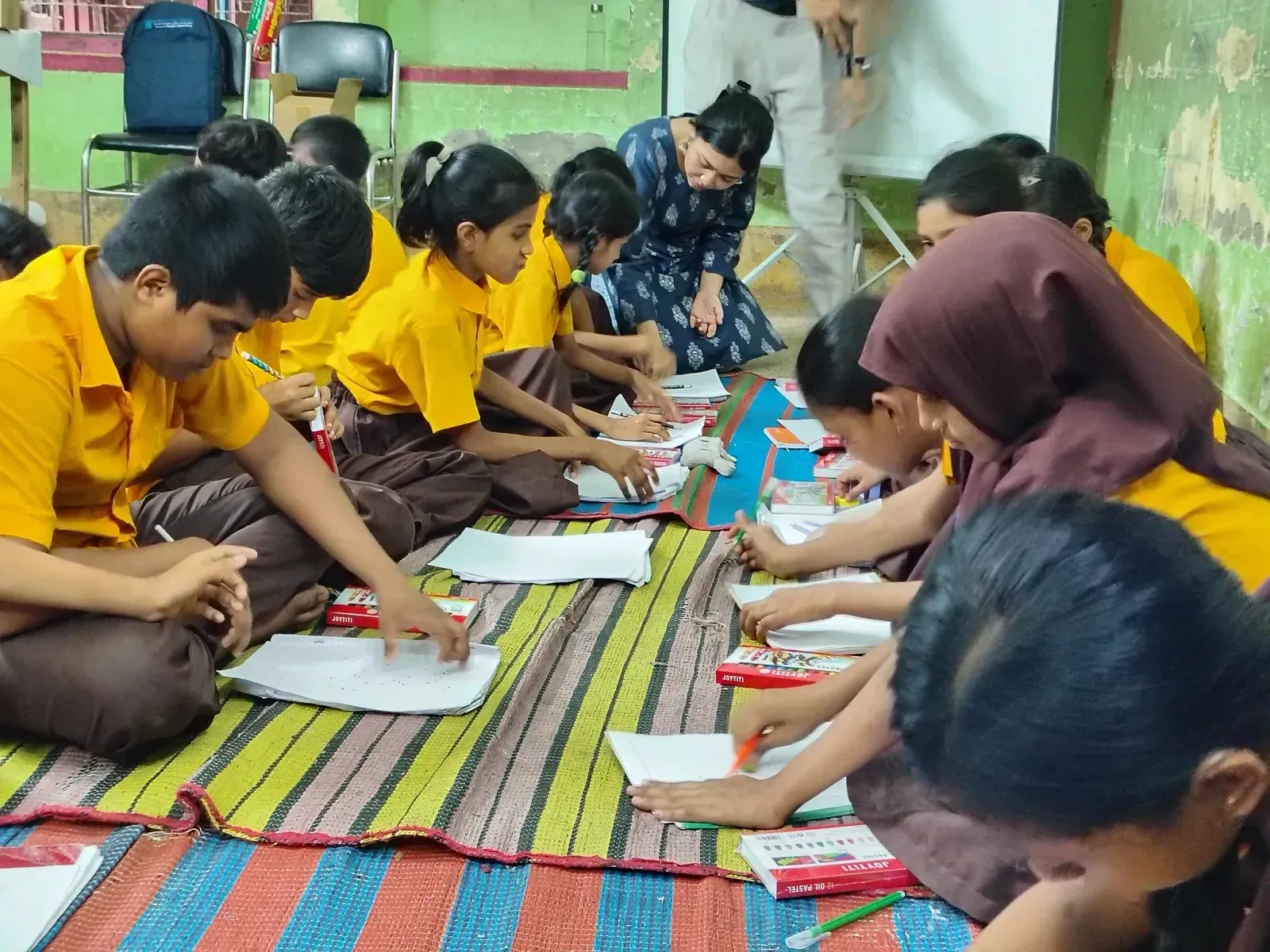 Students drawing on paper while sitting on a mat during the practical activity.