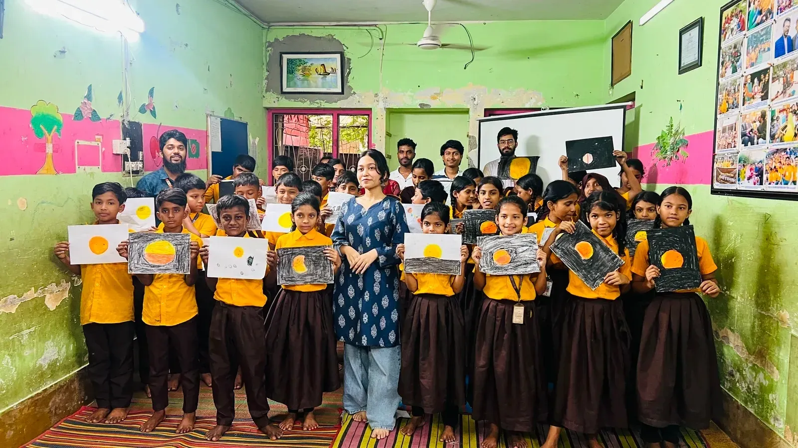 Chayatol students holding up their Sun and eclipse drawings with a Durbin instructor at the close of the outreach session.