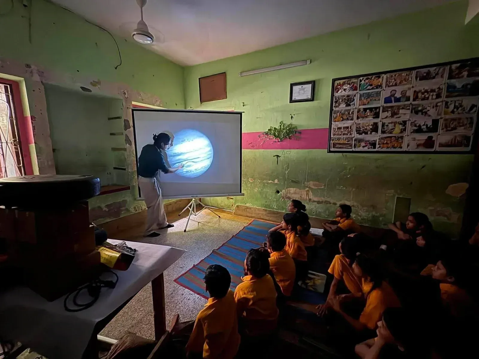 An instructor presents an image of Jupiter and its Great Red Spot on a projector to students seated on the floor.