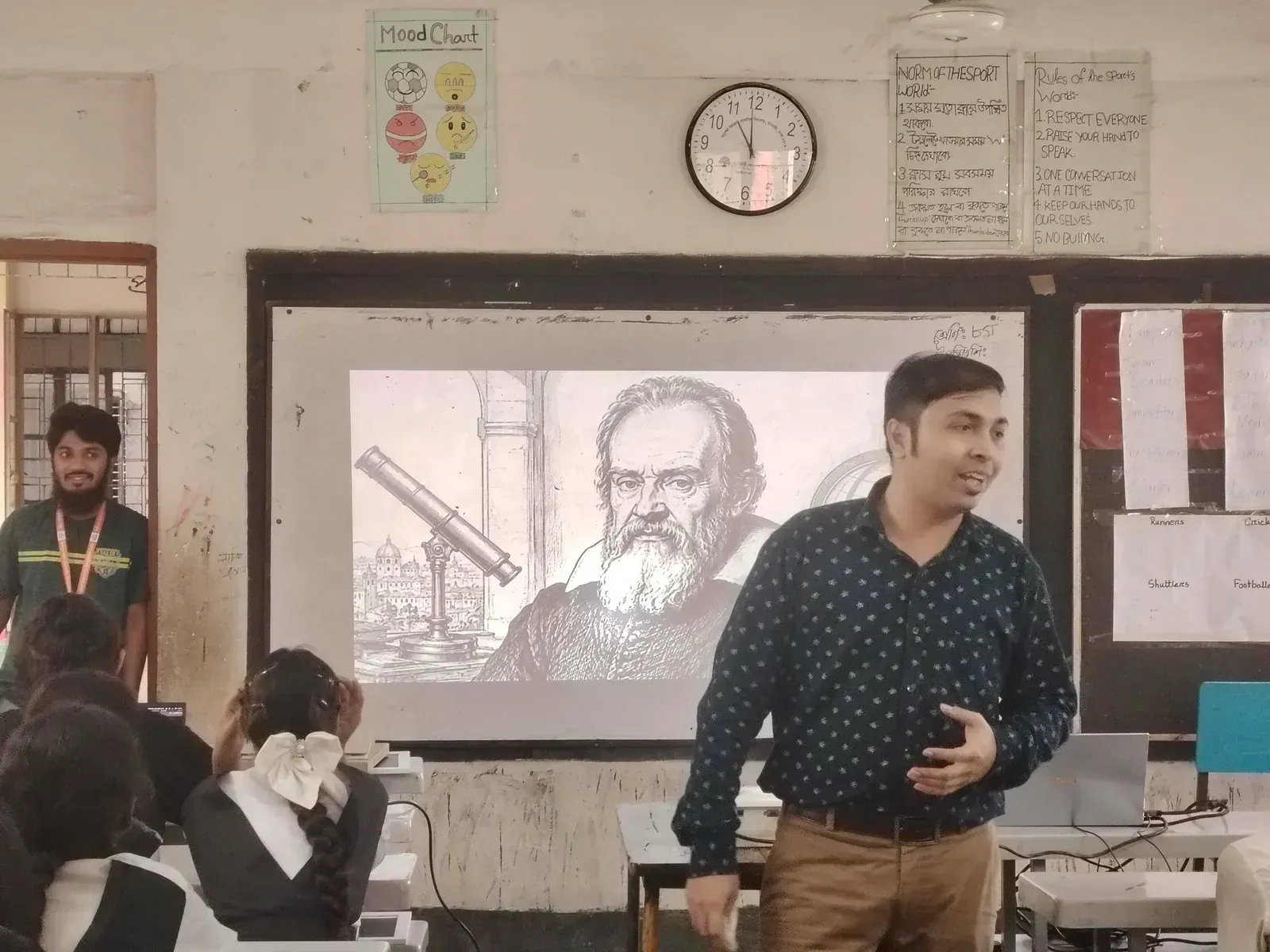 A volunteer leads the storytelling session in front of a slide showing Galileo Galilei and his telescope.