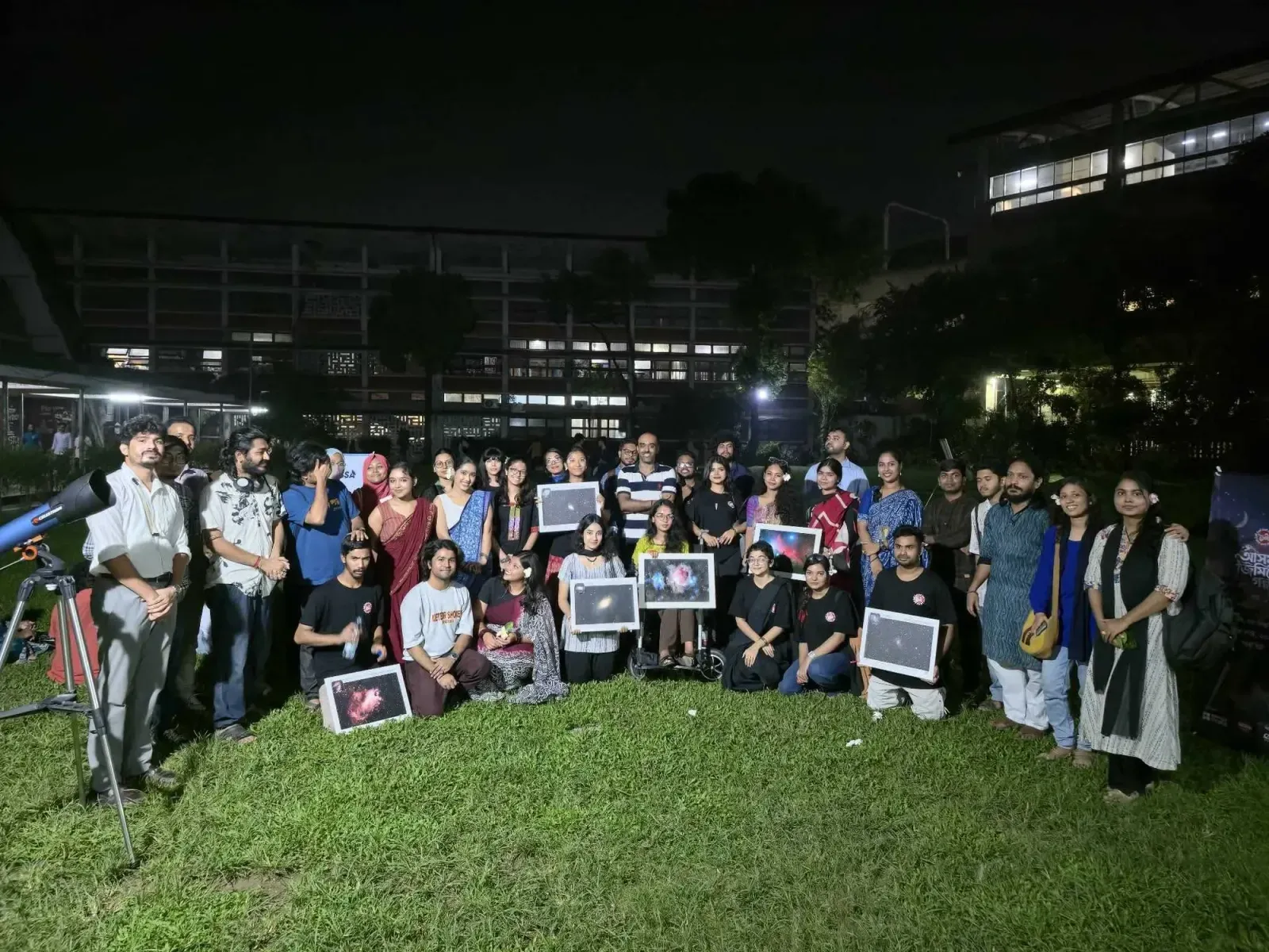 Participants and Durbin volunteers gathered on the TSC lawn at night, several holding framed astrophotographs, with a telescope at the left of the frame.