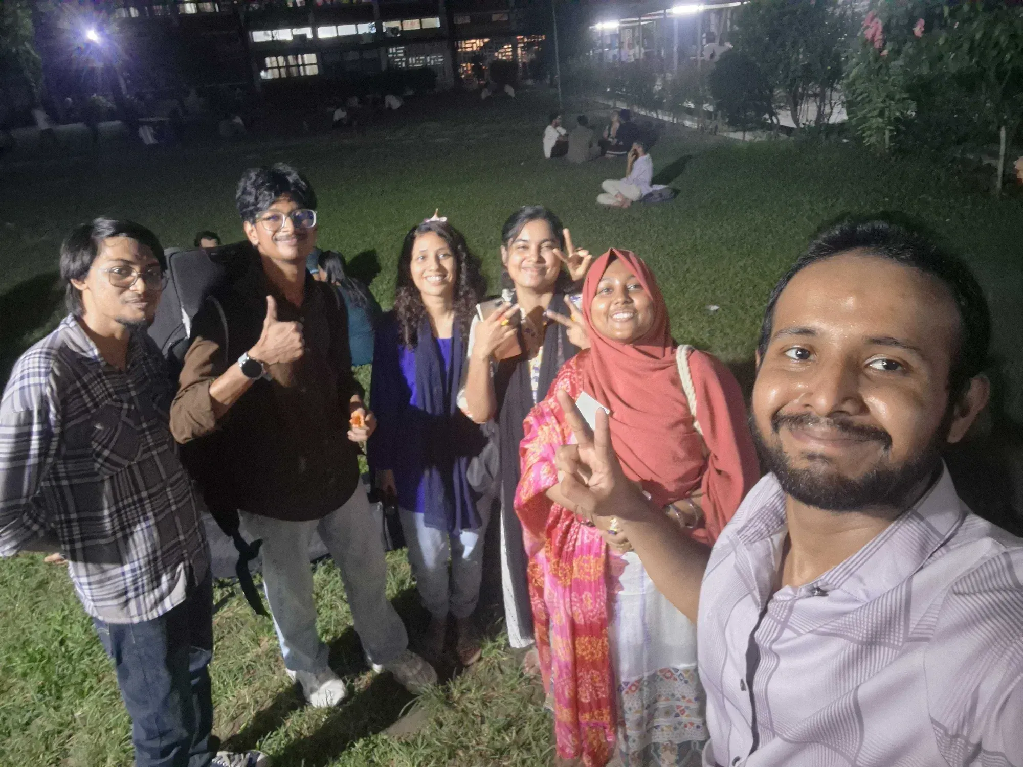Six members of the Durbin and Bhoirobee teams standing together on the TSC lawn at night, smiling at the camera.
