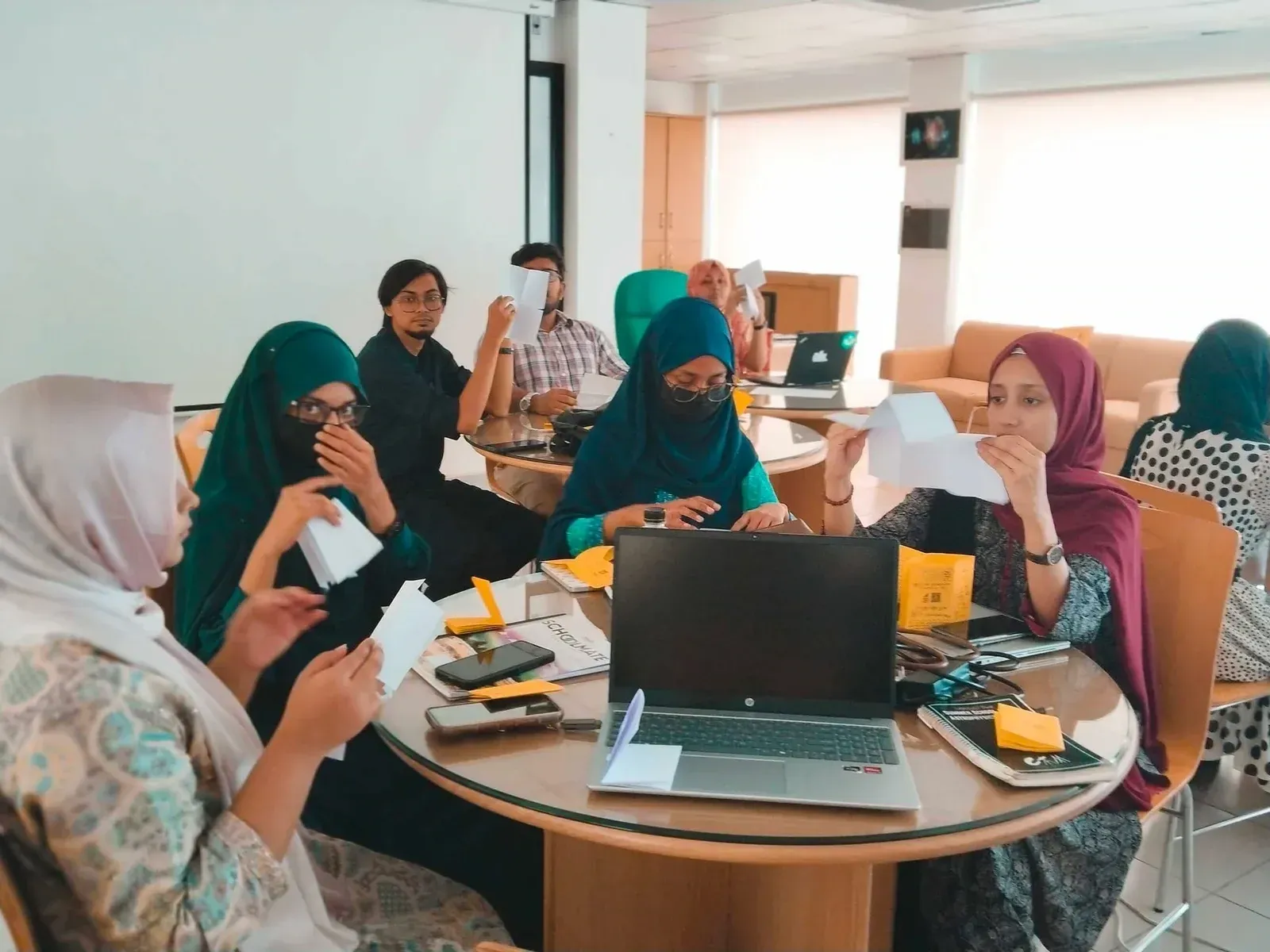 Workshop participants seated at round tables folding paper into zines during Astrophotography Meets Zine Making.